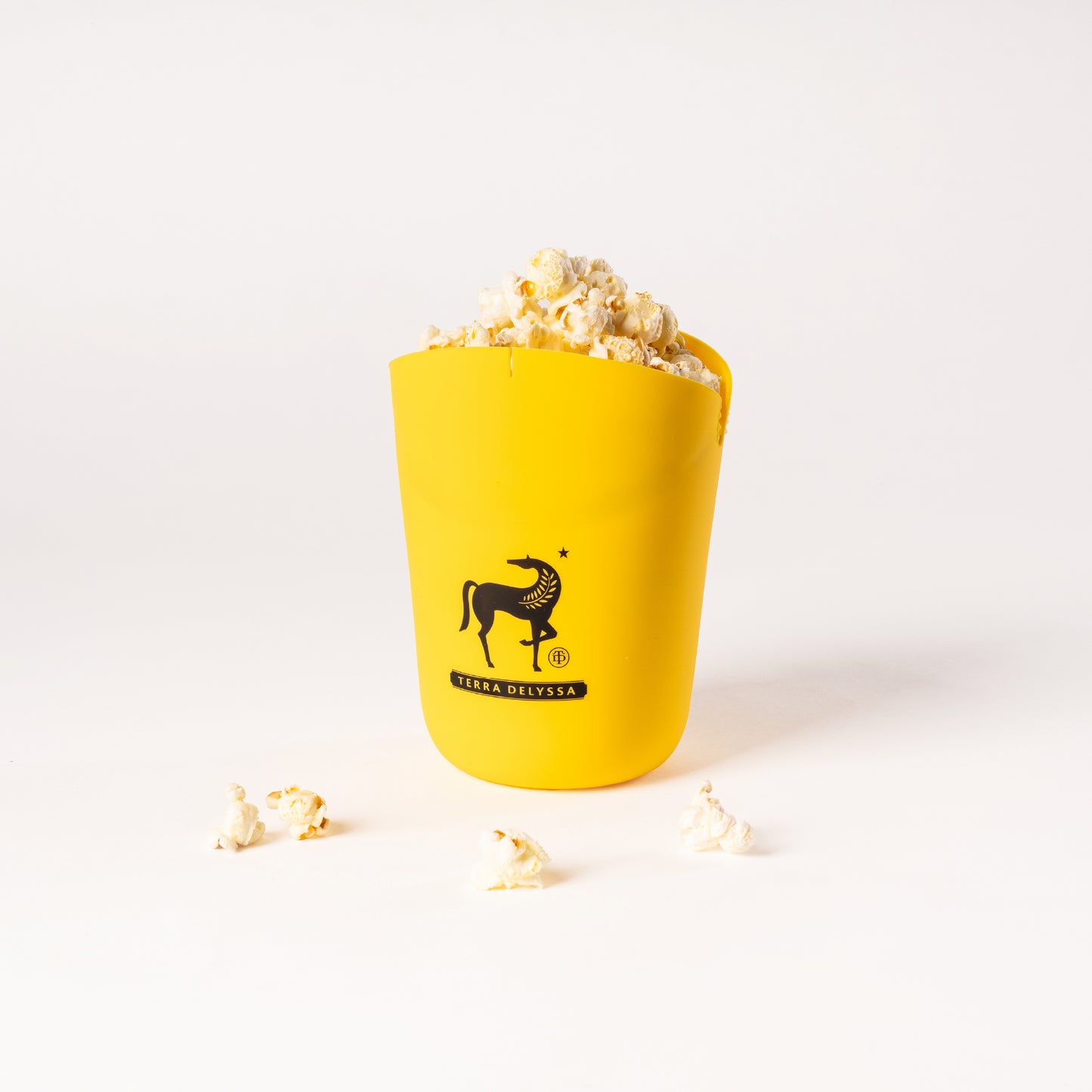 Front view of the yellow Terra Delyssa silicone popcorn popper with popcorn spilling out, featuring the brand’s horse logo prominently displayed.